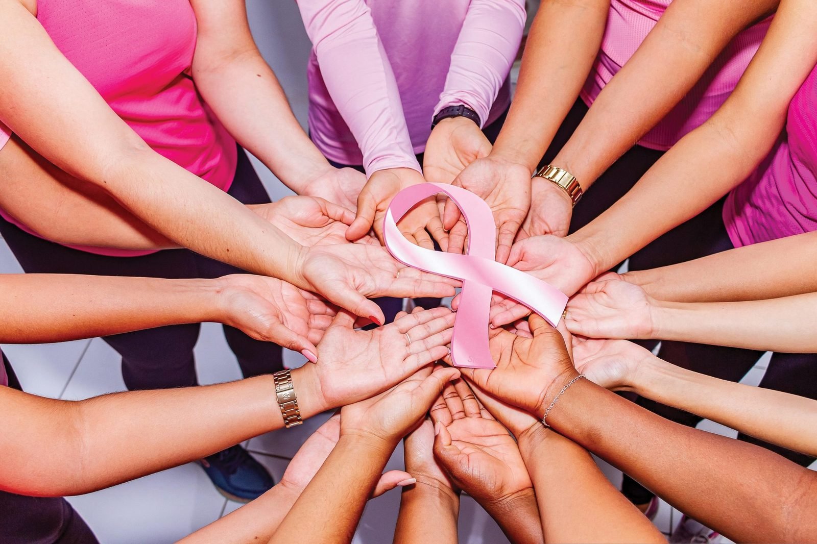 A circle of diverse women joining hands around a pink breast cancer awareness ribbon